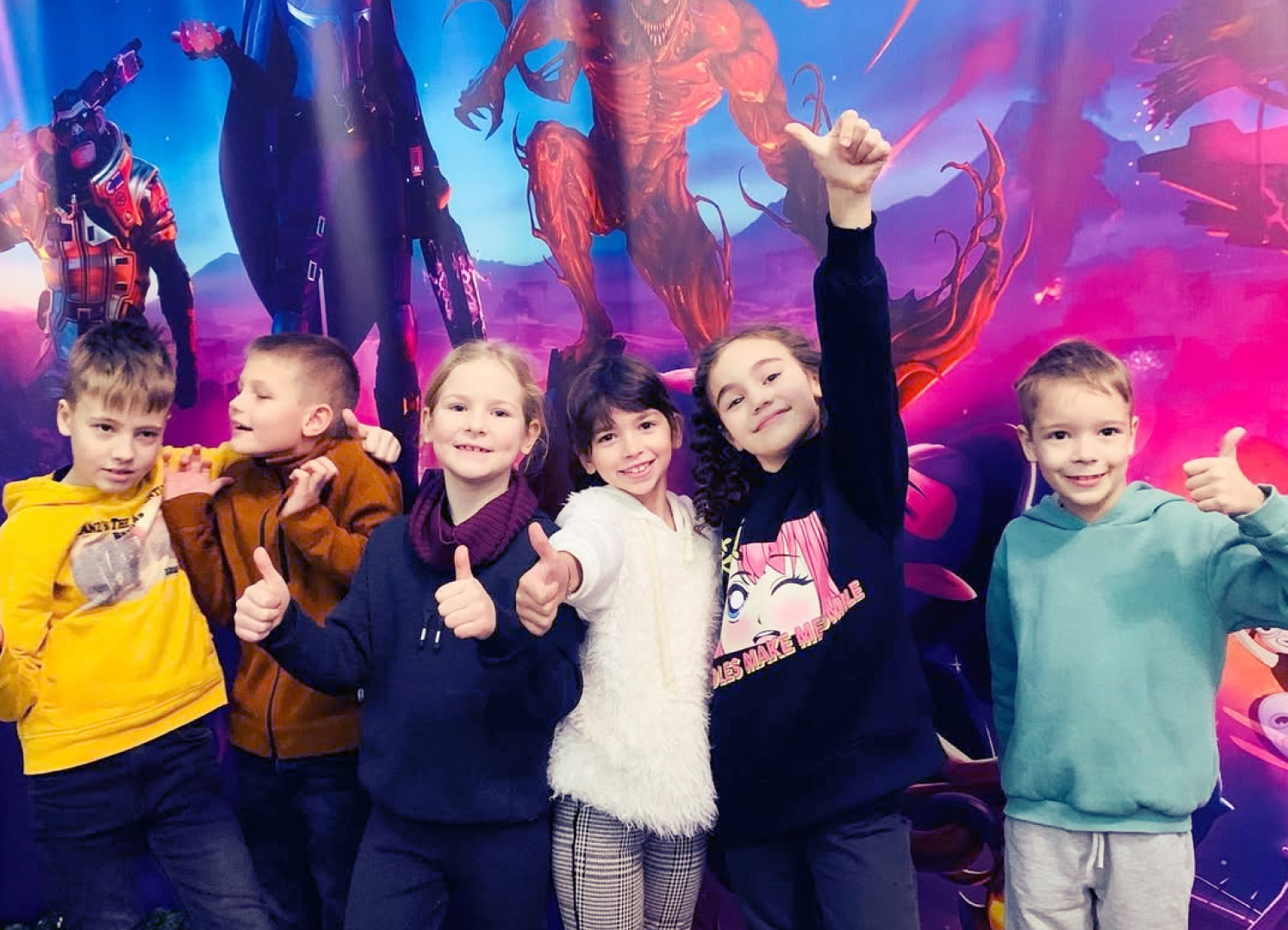 Діти в кінотеатрі на фоні постеру показують знак клас