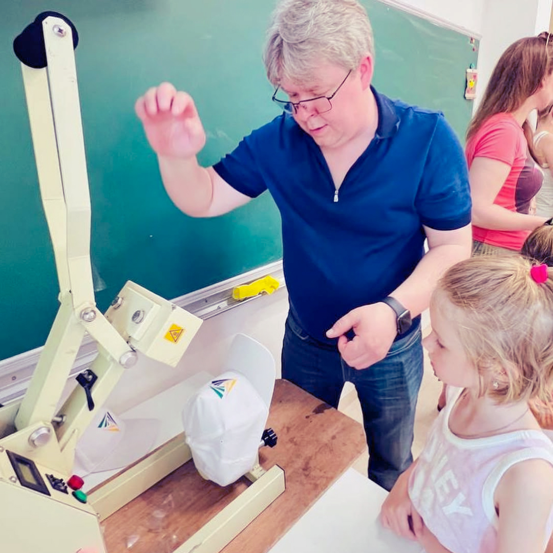 Вчитель показує школярам технологію переносу зображення на кепку за допомогою спеціального пристрою