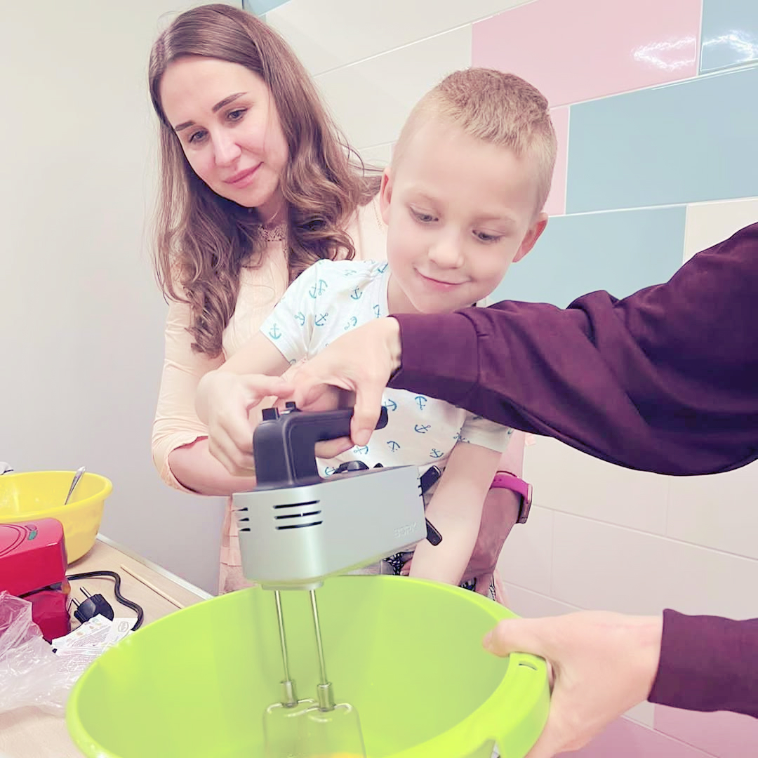 Вчителі у веселій атмосфері вчать учня як працювати із міксером на шкільній кухні