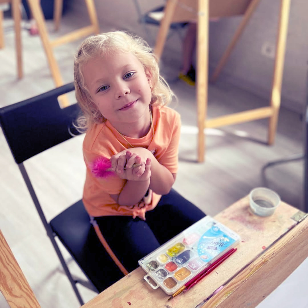 Чарівна дівчинка-учениця молодшої школи на уроці малювання із аквареллю